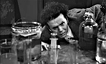 Captura de tela do filme Maniac (1934), em domínio público. Um personagem olha para garrafas de vidro sobre uma bancada.