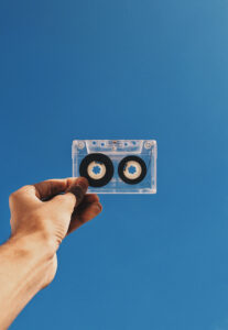 Fotografia de uma mão segurando uma fita cassete contra um fundo azul. Fotografia de uma mão segurando uma fita cassete contra um fundo azul.