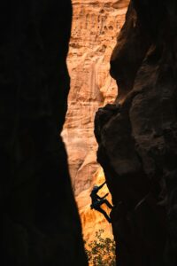 Fotografia de uma pessoa escalando um cânion. A pessoa está no meio do trajeto, rumando ao topo.